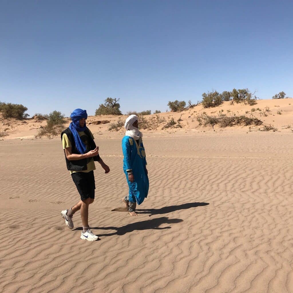 Deux hommes marchant dans le désert, l'un en turban bleu, l'autre en turban blanc