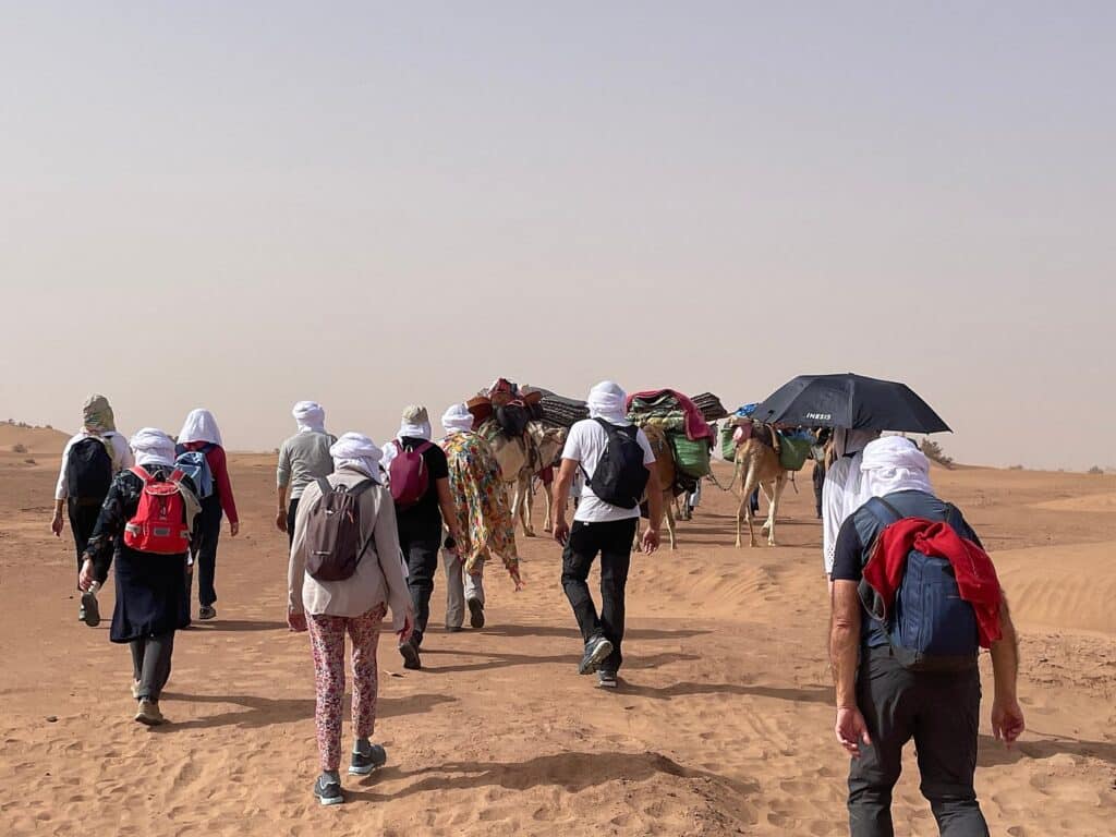 Groupe de randonneurs marchant avec des dromadaires dans les dunes de l'Erg Chebbi